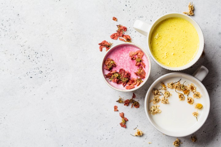 Different types of moon milk: rose flower, golden turmeric and chamomile in white cups, top view. Ayurveda drink, healthy lifestyle, remedy for insomnia.