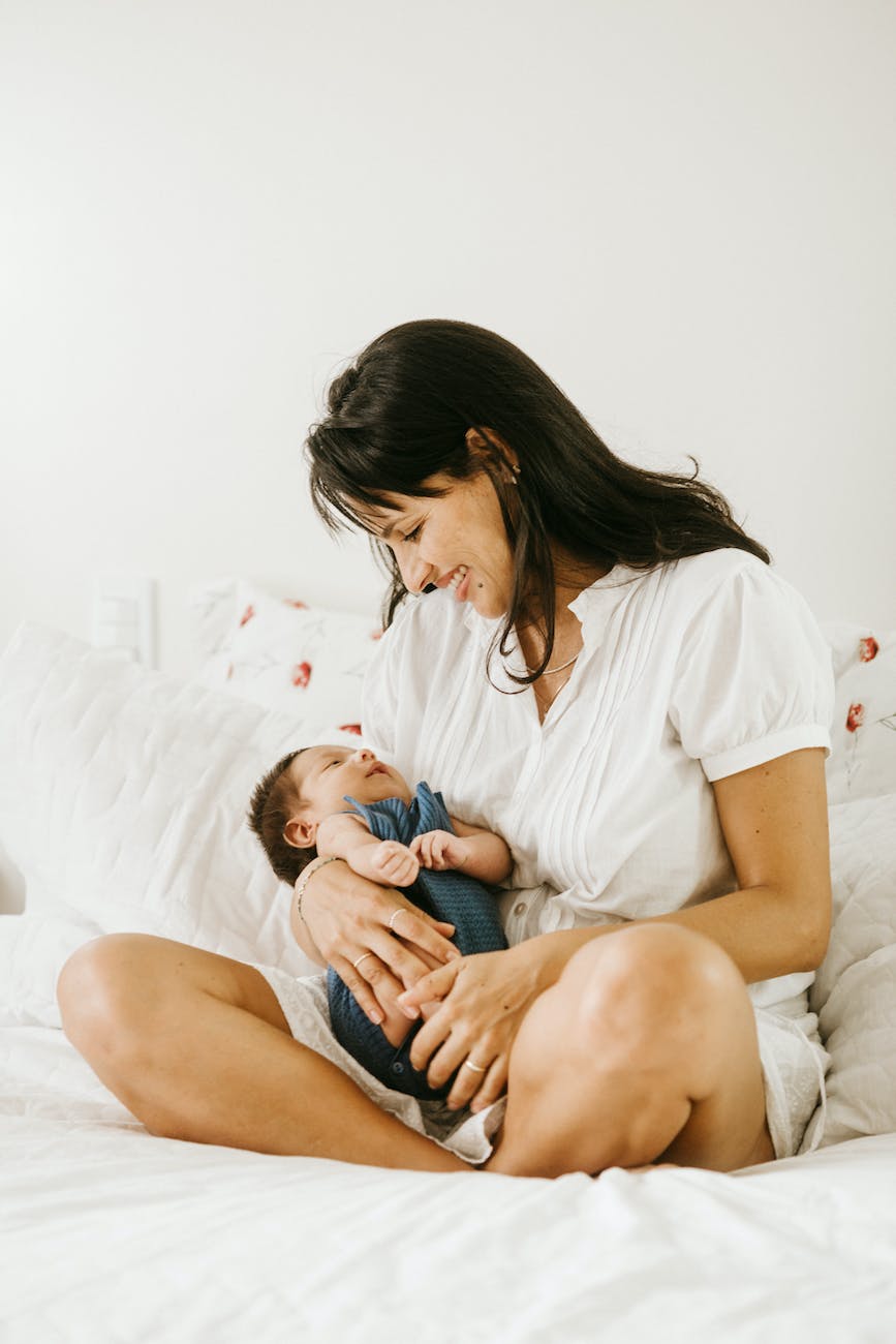 photo of a smiling woman carrying her baby while sitting on a bed mother and baby postpartum