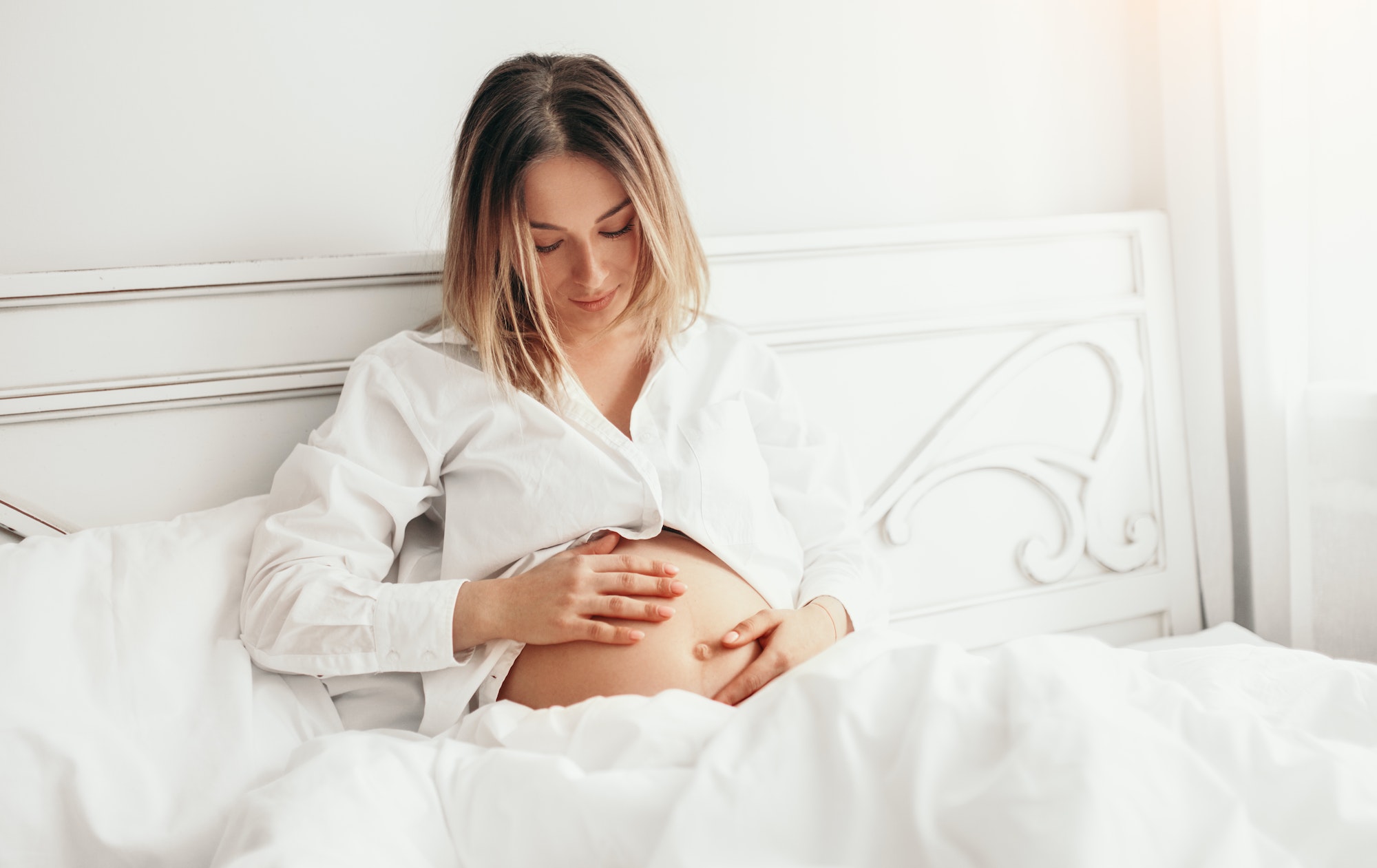 early pregnancy Pregnant woman touching belly on bed