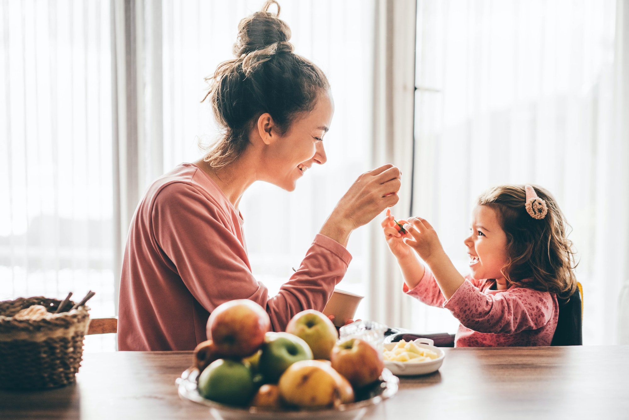 Mother feeding happy toddler girl with a spoon for an article about the importance of probiotics for toddlers for gut health in toddlers