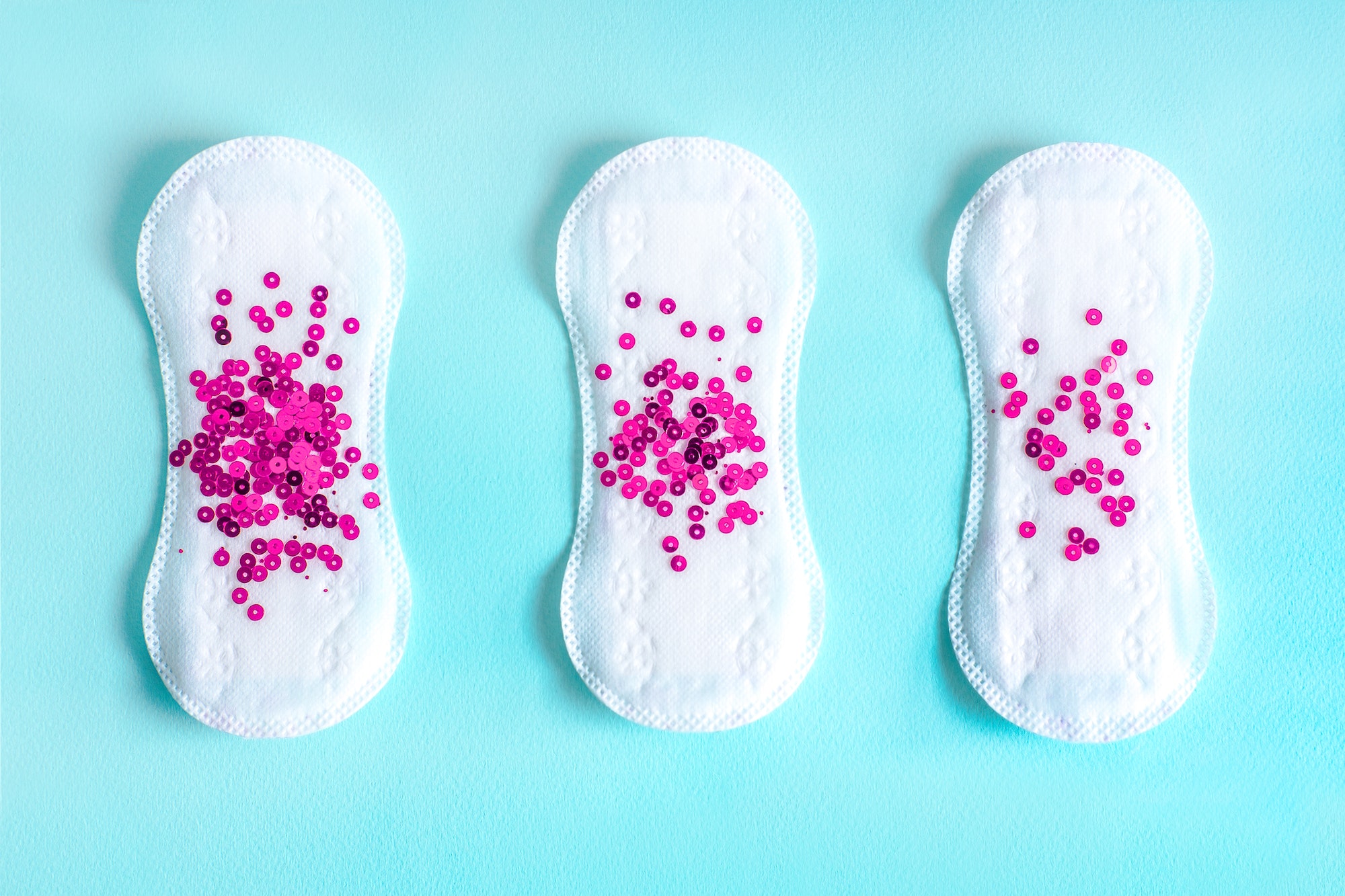 Postpartum Bleeding - Menstrual pad with bright purple sequins on a blue colored background.